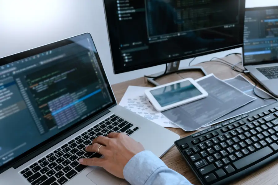 Person coding on a laptop with multiple screens and devices.