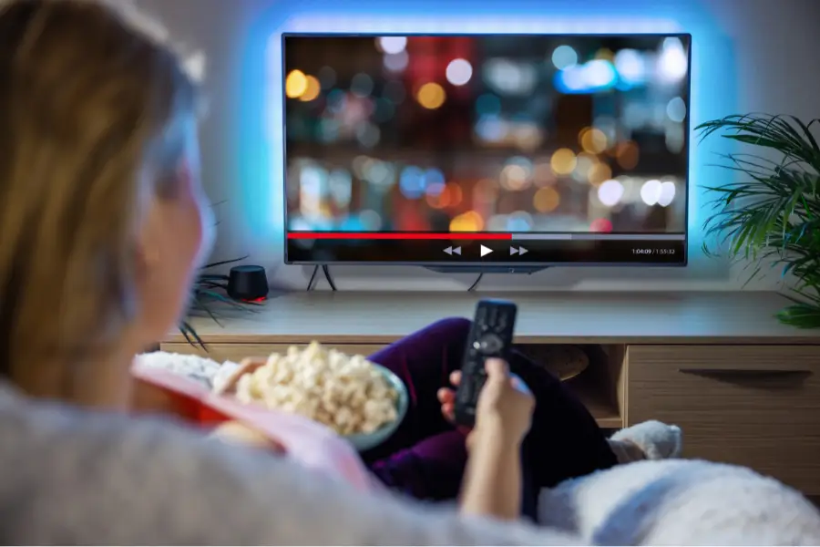 Person watching TV with popcorn and remote.